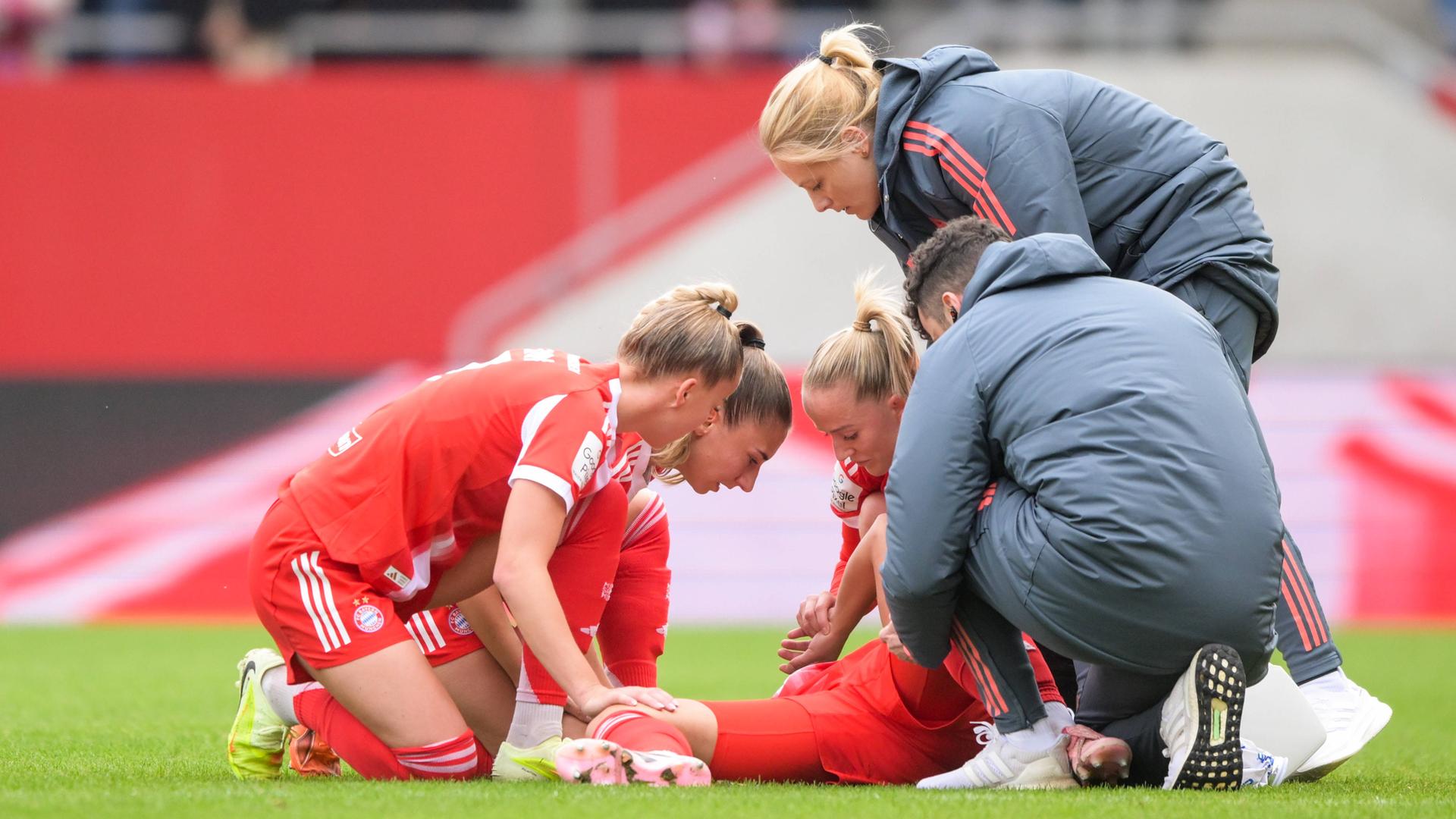 Fußballerin Lena Oberdorf liegt auf dem Spielfeldbogen, umgeben von besorgten Kolleginnen und einem Kollegen, nachdem sie sich während eines Spiels verletzte.