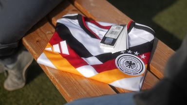 Ein zusammengefaltetes Trikot der deutschen Fußball-Nationalmannschaft, an dem ein Preisschild hängt, liegt auf einer Bank. 
