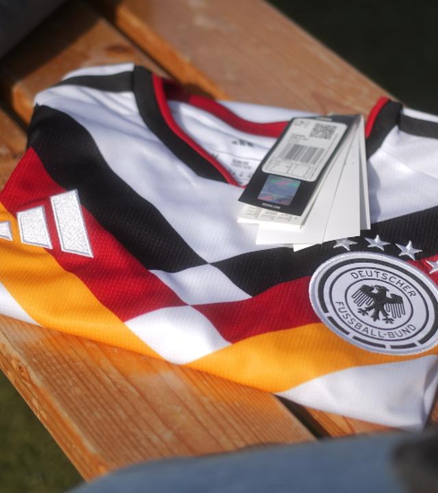 Ein zusammengefaltetes Trikot der deutschen Fußball-Nationalmannschaft, an dem ein Preisschild hängt, liegt auf einer Bank. 