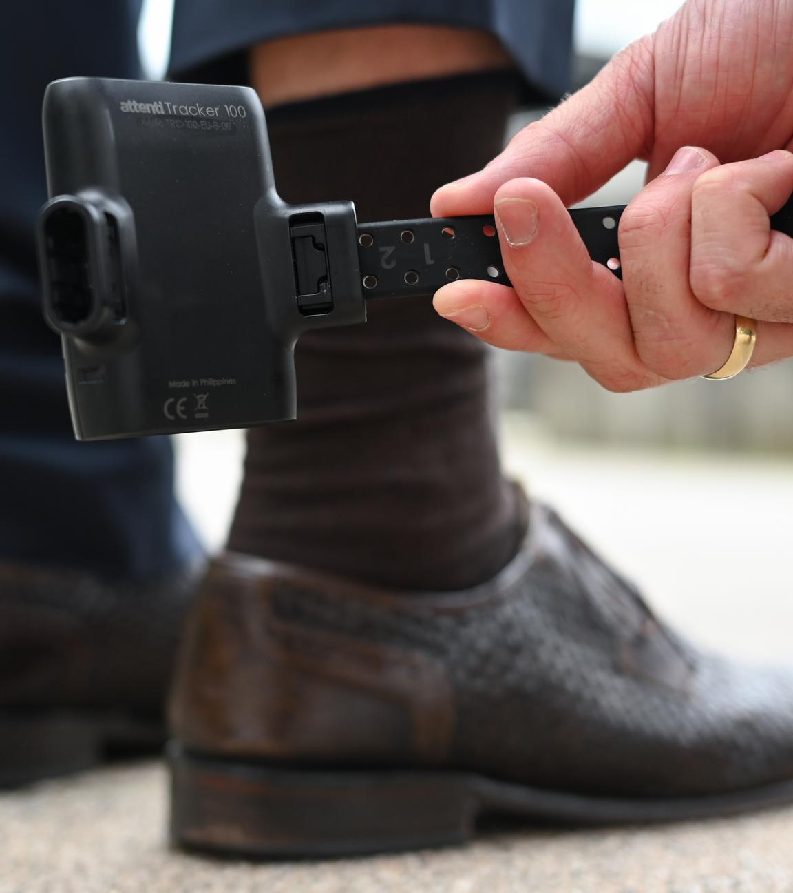 Ein Mann hält zu Demonstrationszwecken eine elektronische Aufenthaltsüberwachung, bekannt als elektronische Fußfessel, vor das Bein eines Probanden. 