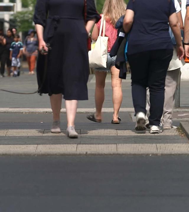 Beine von Menschen, die eine Straße überqueren, ein Hund an der Leine
