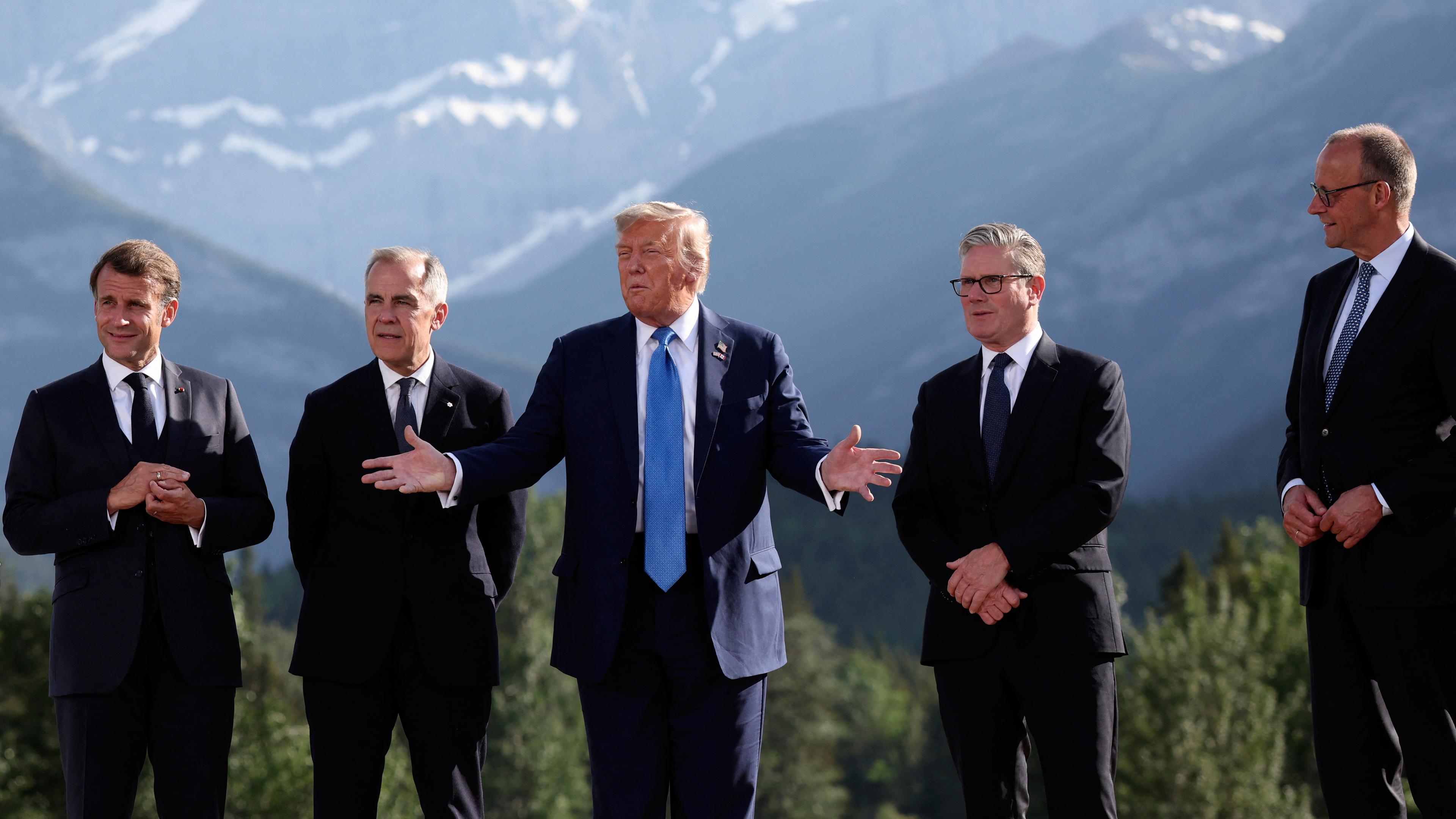 Macro, Carney, Trump, Starmer und Merz stehen nebeneinander, Trump spricht und gestikuliert, im Hintergrund ein Bergpanorama