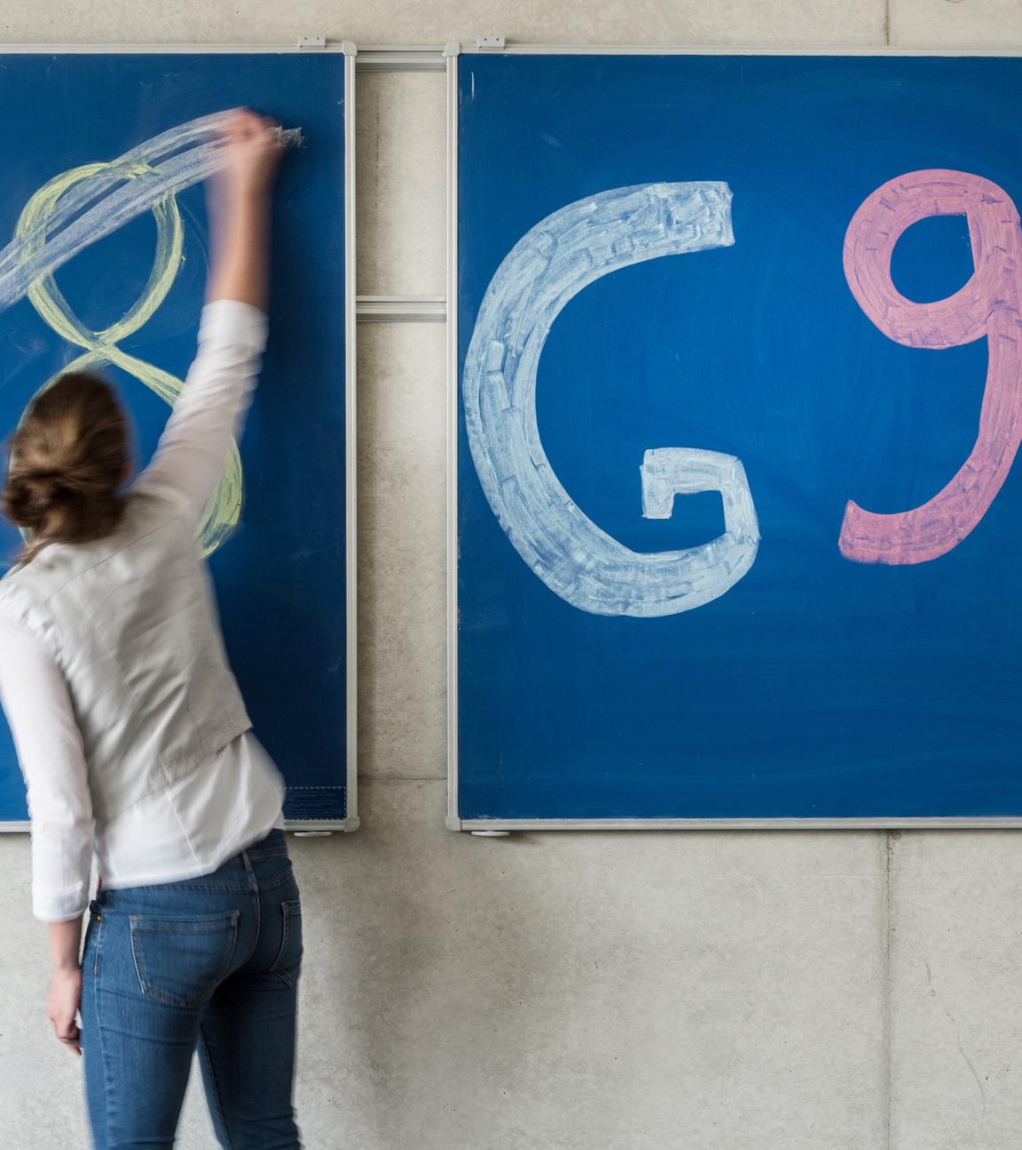 Eine Schülerin der Oberstufe streicht an einem Gymnasium den Schriftzug "G8" an einer Tafel durch, daneben lässt sie "G9" unberührt.