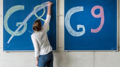 Eine Schülerin der Oberstufe streicht an einem Gymnasium den Schriftzug "G8" an einer Tafel durch, daneben lässt sie "G9" unberührt.