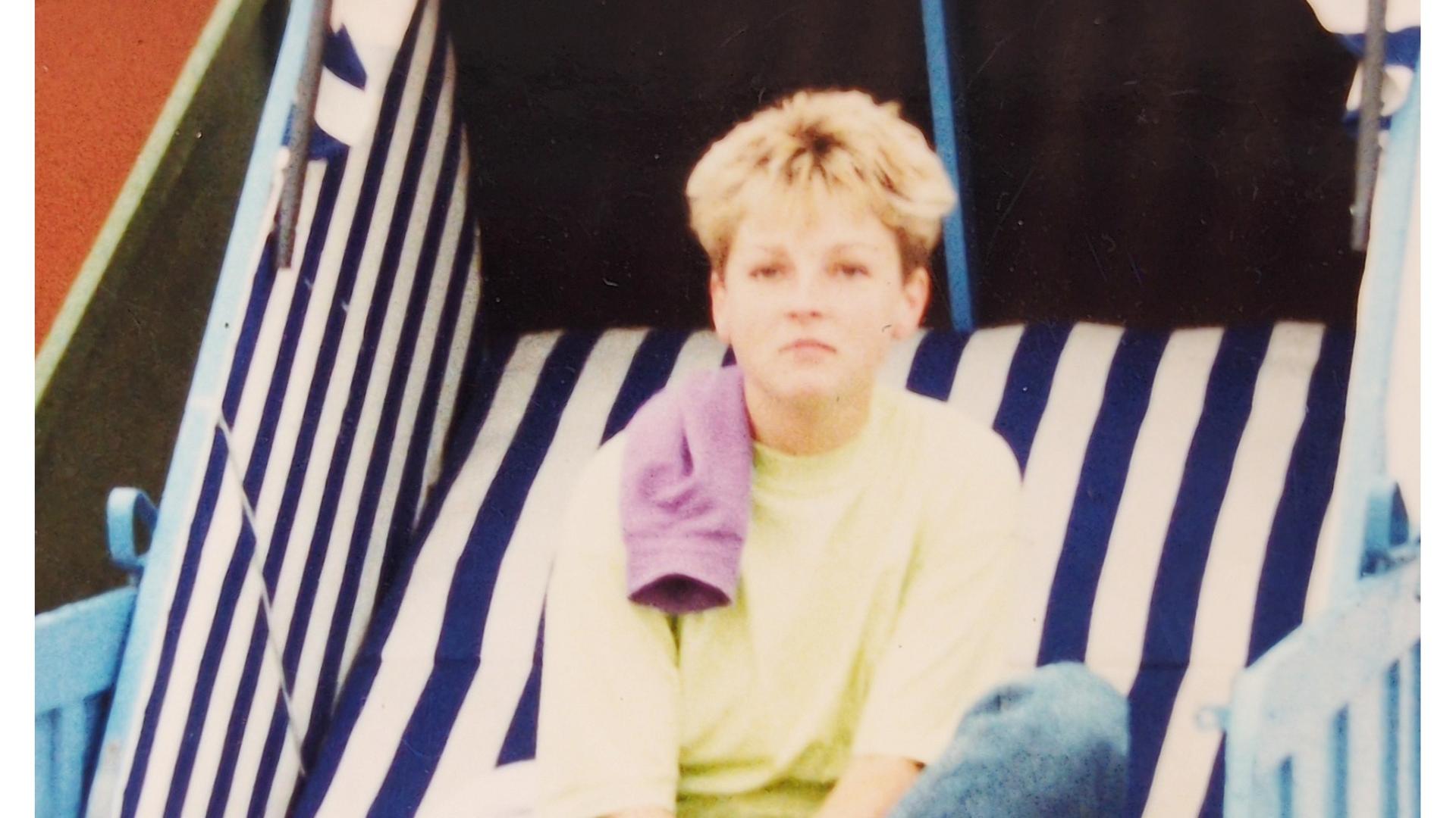 Eine Person mit kurzen Haaren sitzt in einem gestreiften Strandkorb.