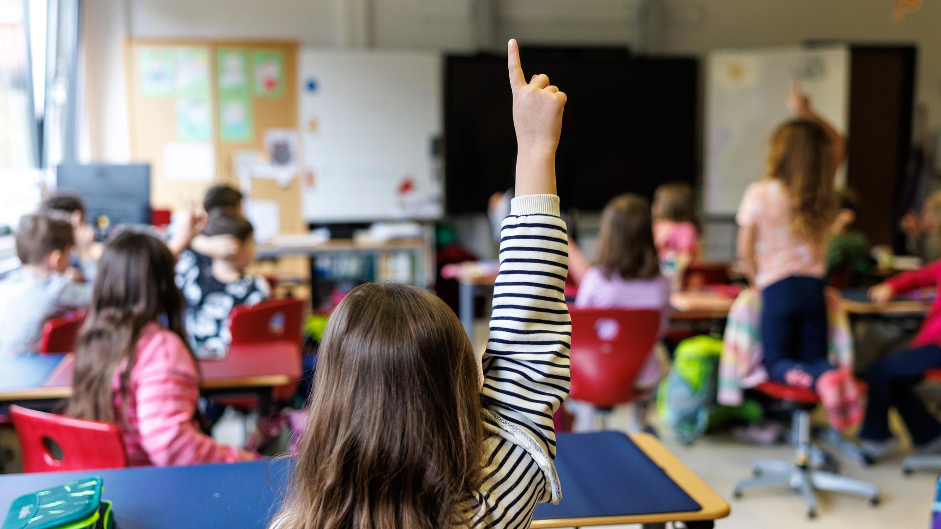 Ein Grundschulkind meldet sich in einem Klassenraum voller Kinder während des Unterrichtes.