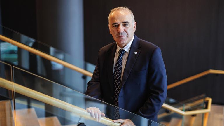 Ein Mann mit spärlichen grauen Haaren, gekleidet in einen dunkelblauen Anzug, steht auf einer Treppe.