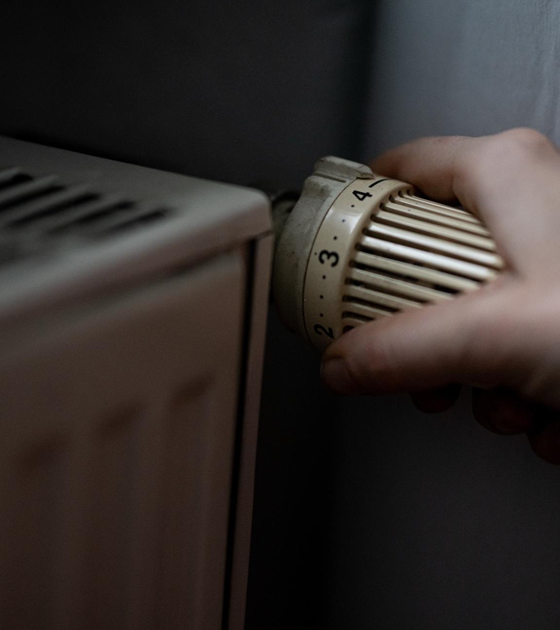 Eine Person dreht am Thermostat einer Heizung. 