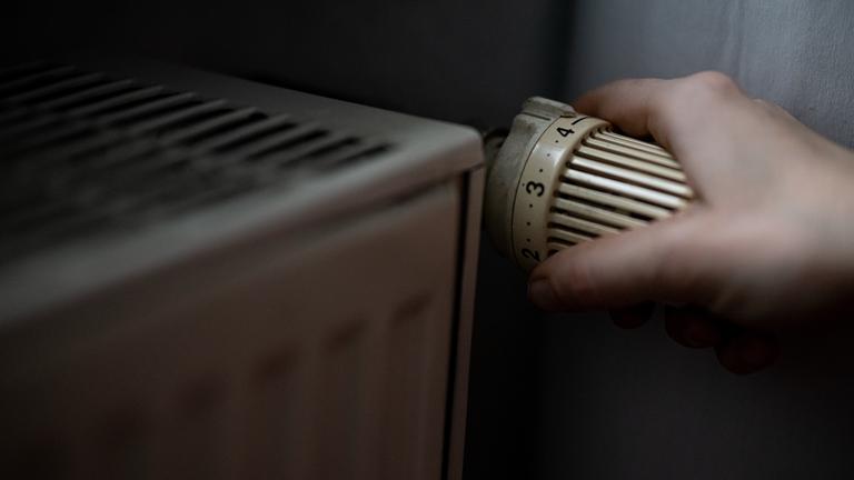 Eine Person dreht am Thermostat einer Heizung. 