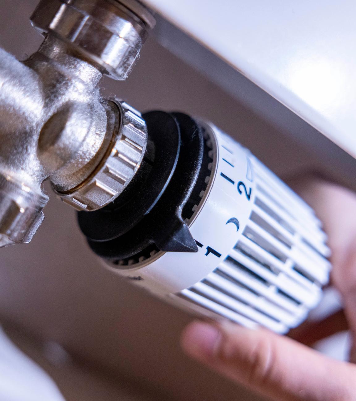 Eine Person dreht am Thermostat einer Heizung. 