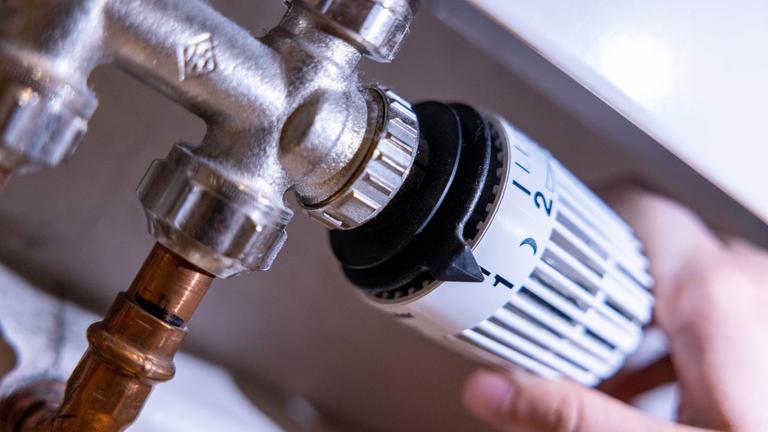 Eine Person dreht am Thermostat einer Heizung. 