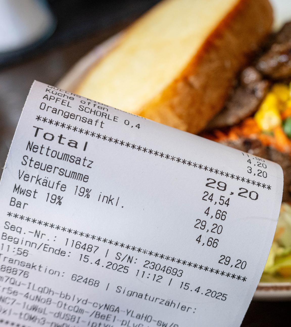 Eine Rechnung der Mehrwertsteuer neben einem vollen Teller in einem Restaurant
