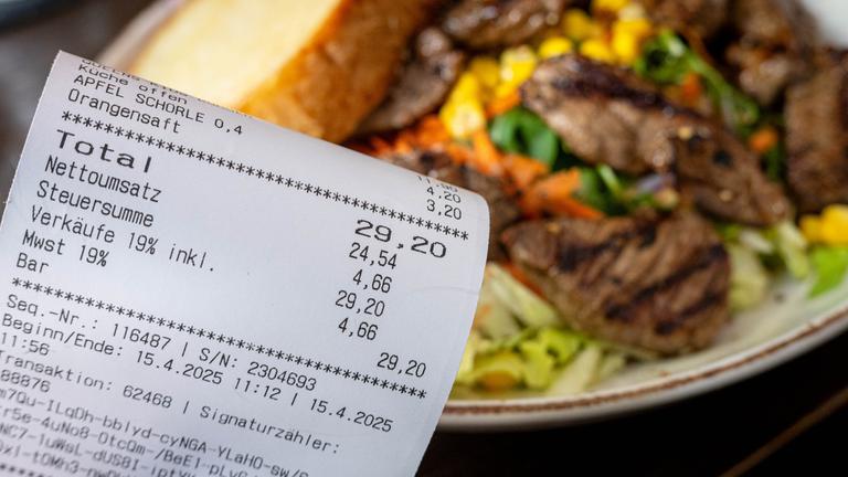Eine Rechnung der Mehrwertsteuer neben einem vollen Teller in einem Restaurant