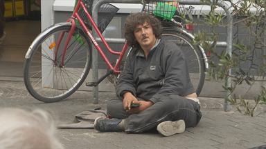 Ein Bettler sitzt ruhig in der Fußgängerzone.