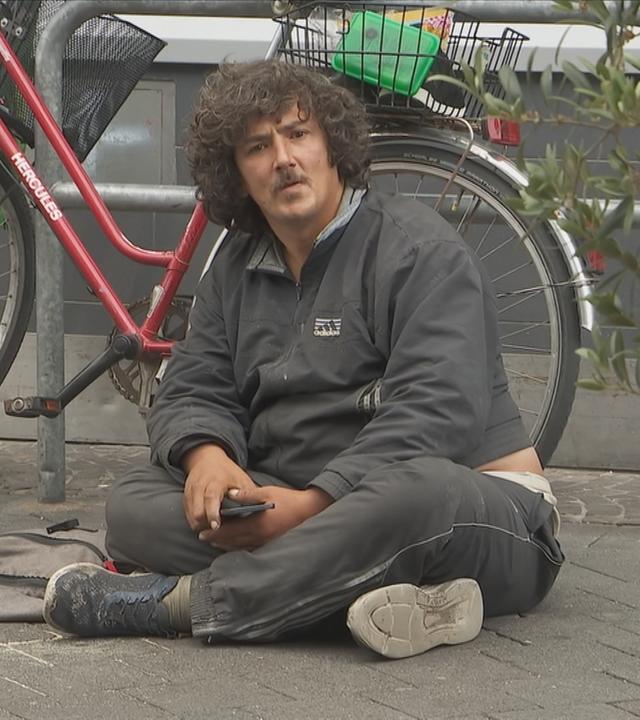 Ein Bettler sitzt ruhig in der Fußgängerzone.