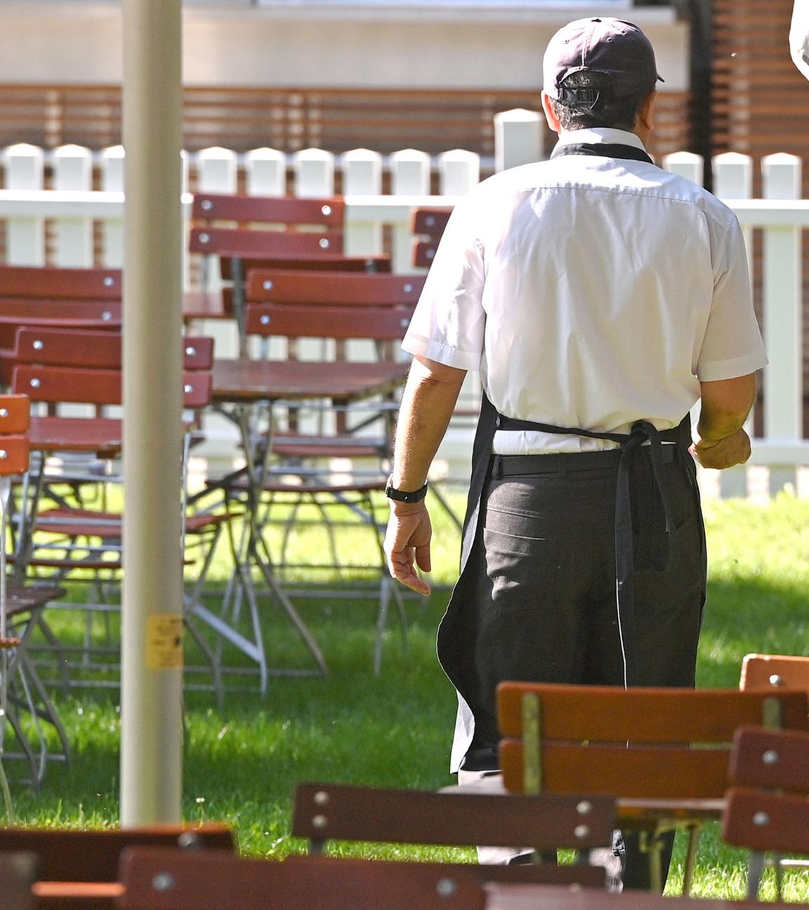 Eine männliche Servicekraft geht durch leere Tischreihen mit freien Stühlen. (Archiv)