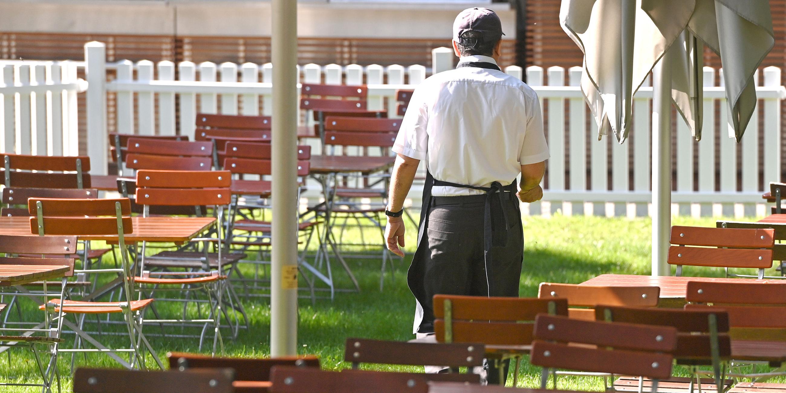 Eine männliche Servicekraft geht durch leere Tischreihen mit freien Stühlen. (Archiv)