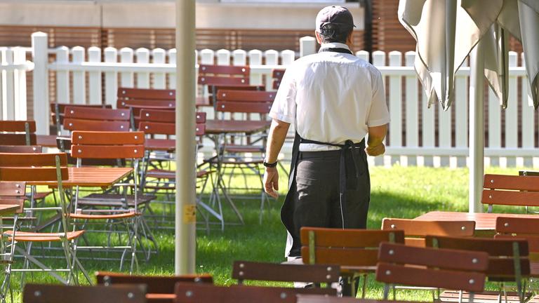 Eine männliche Servicekraft geht durch leere Tischreihen mit freien Stühlen. (Archiv)