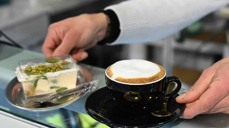 Symbolbild: Ein Verkäufer gibt in der Eisdiele Dolce eine Tasse mit Cappuccino und ein Tiramisu über den Tresen.