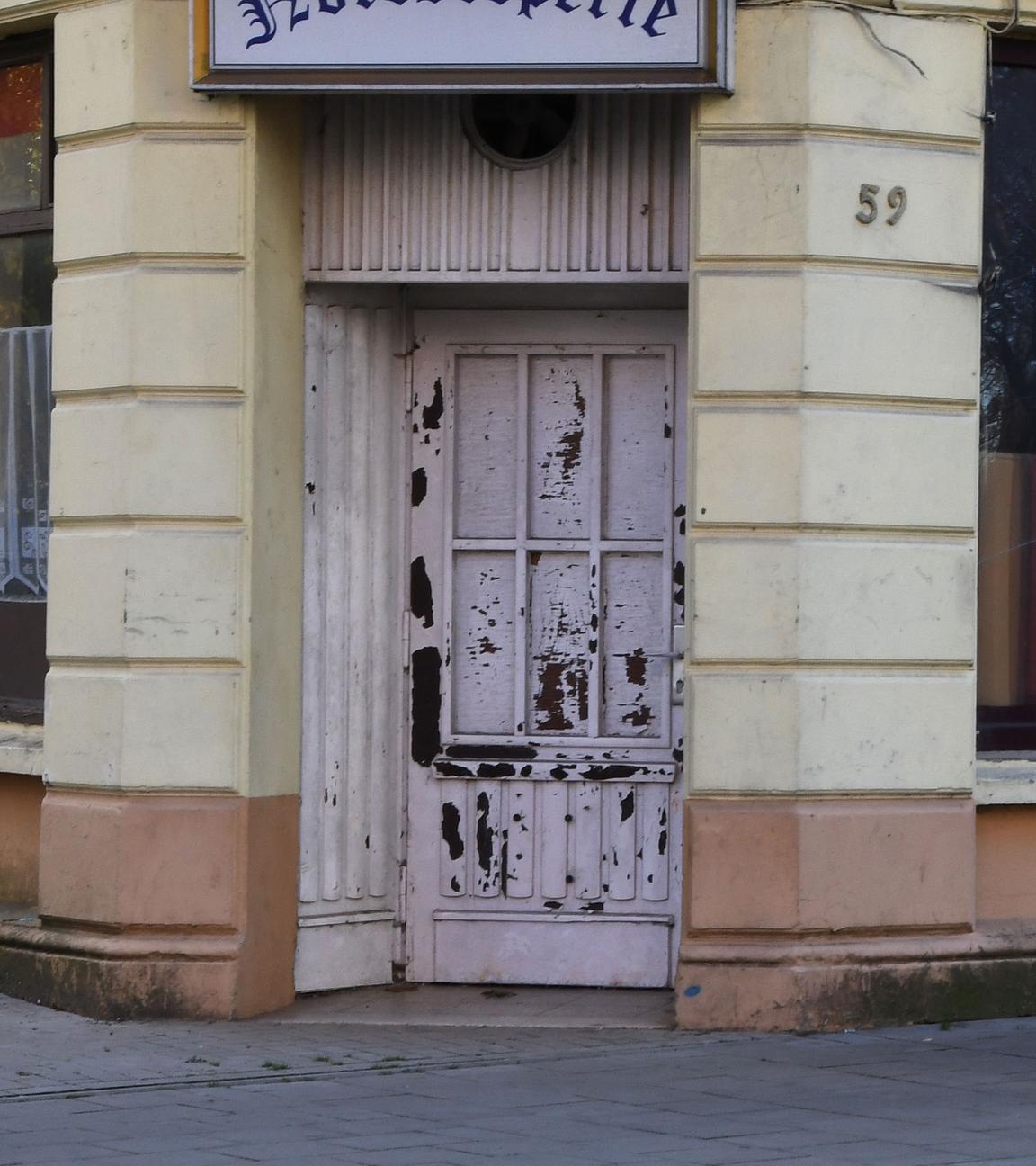 Ein Mann geht an einem kaputten Fenster einer geschlossenen Kneipe entlang.
