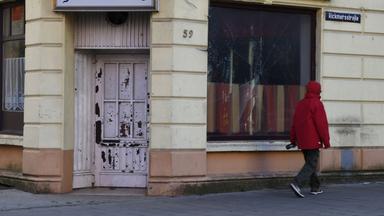 Ein Mann geht an einem kaputten Fenster einer geschlossenen Kneipe entlang.