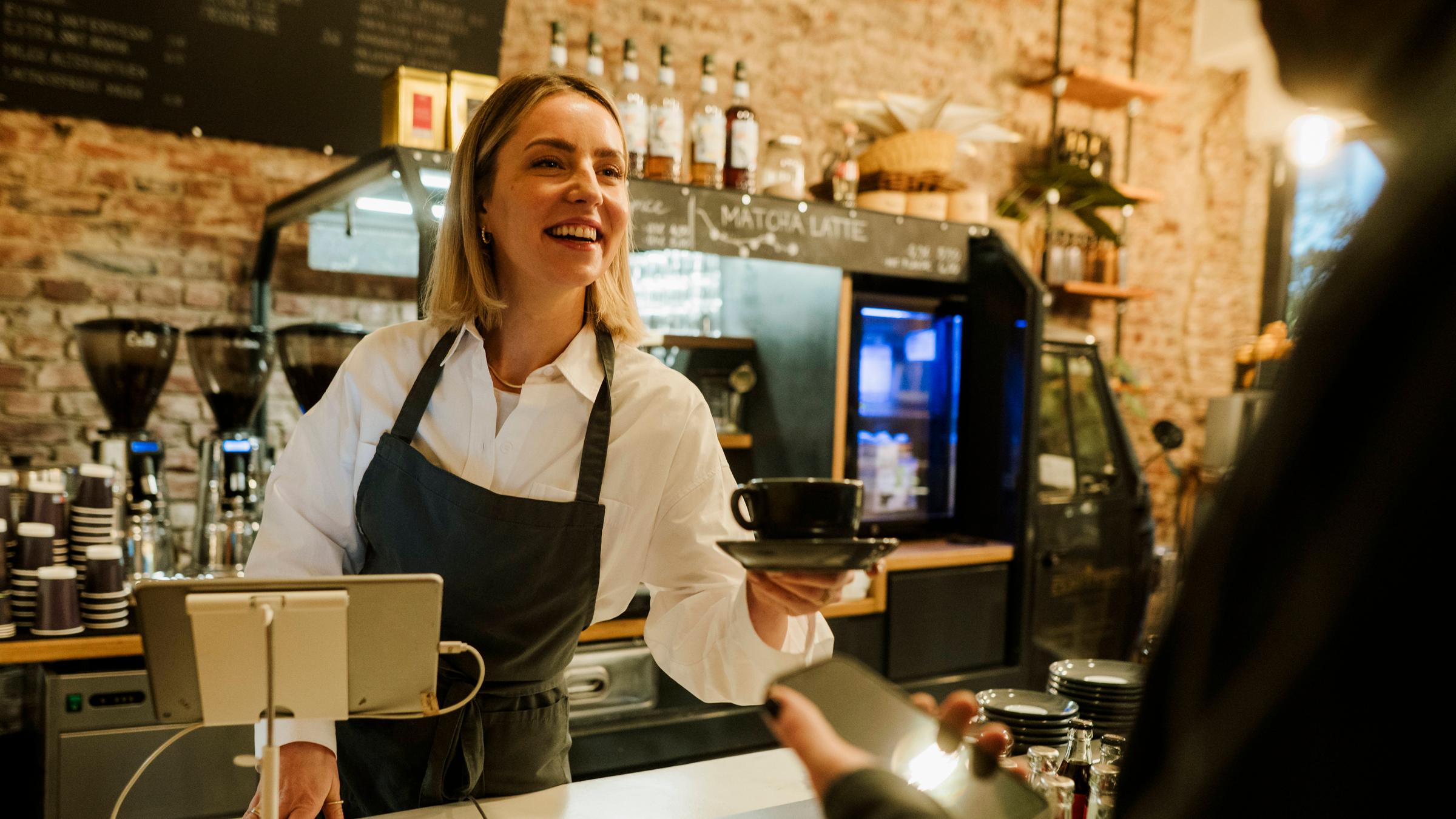 Eine Barista reicht einer Kundin einen Kaffee.