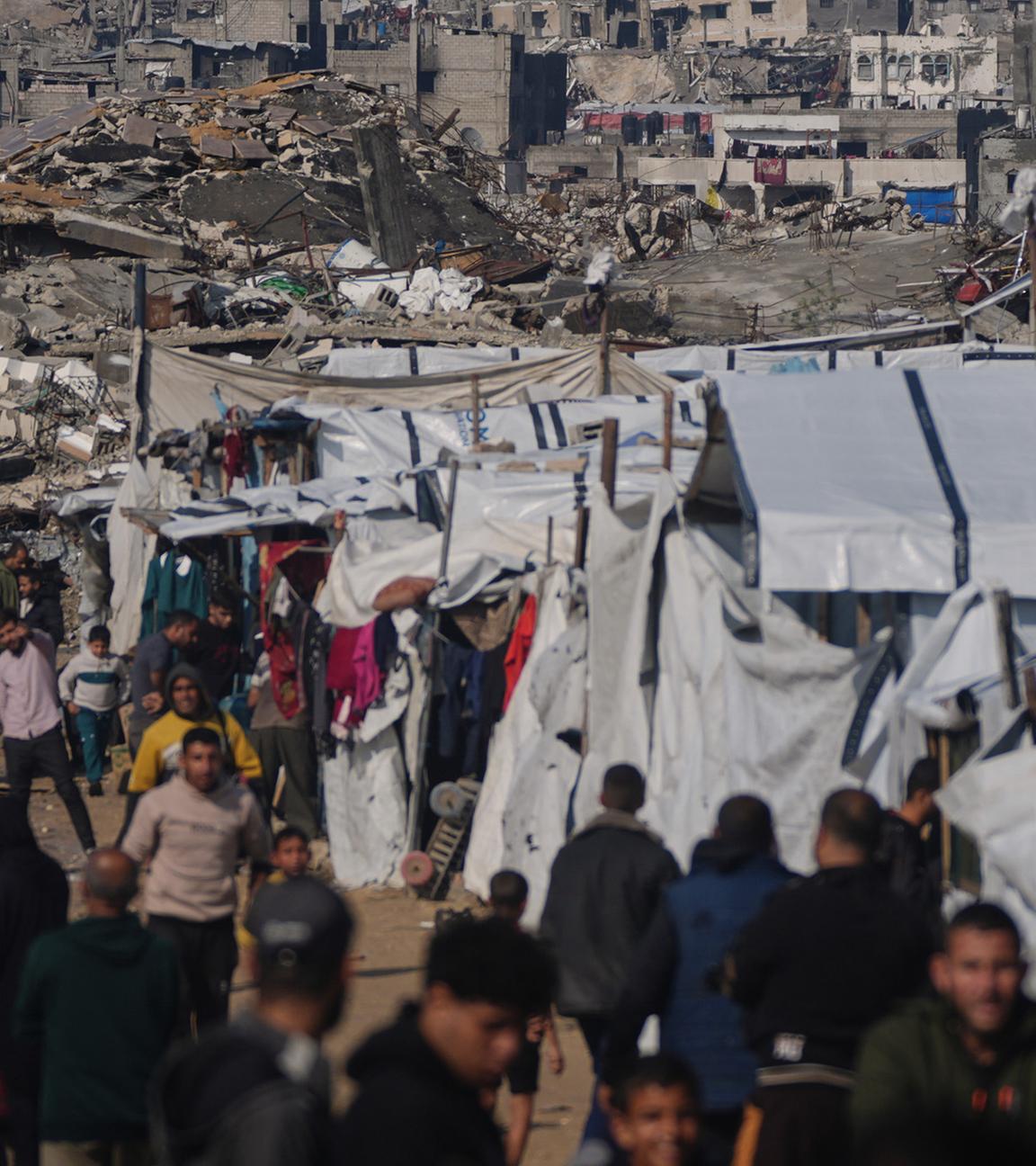 Palästinenser gehen an einem Zeltlager vorbei durch eine Straße in Gaza-Stadt, vor im Hintergrund zerstörten Gebäuden nach israelischen Luft- und Bodeneinsätzen, am 17. Dezember 2025.