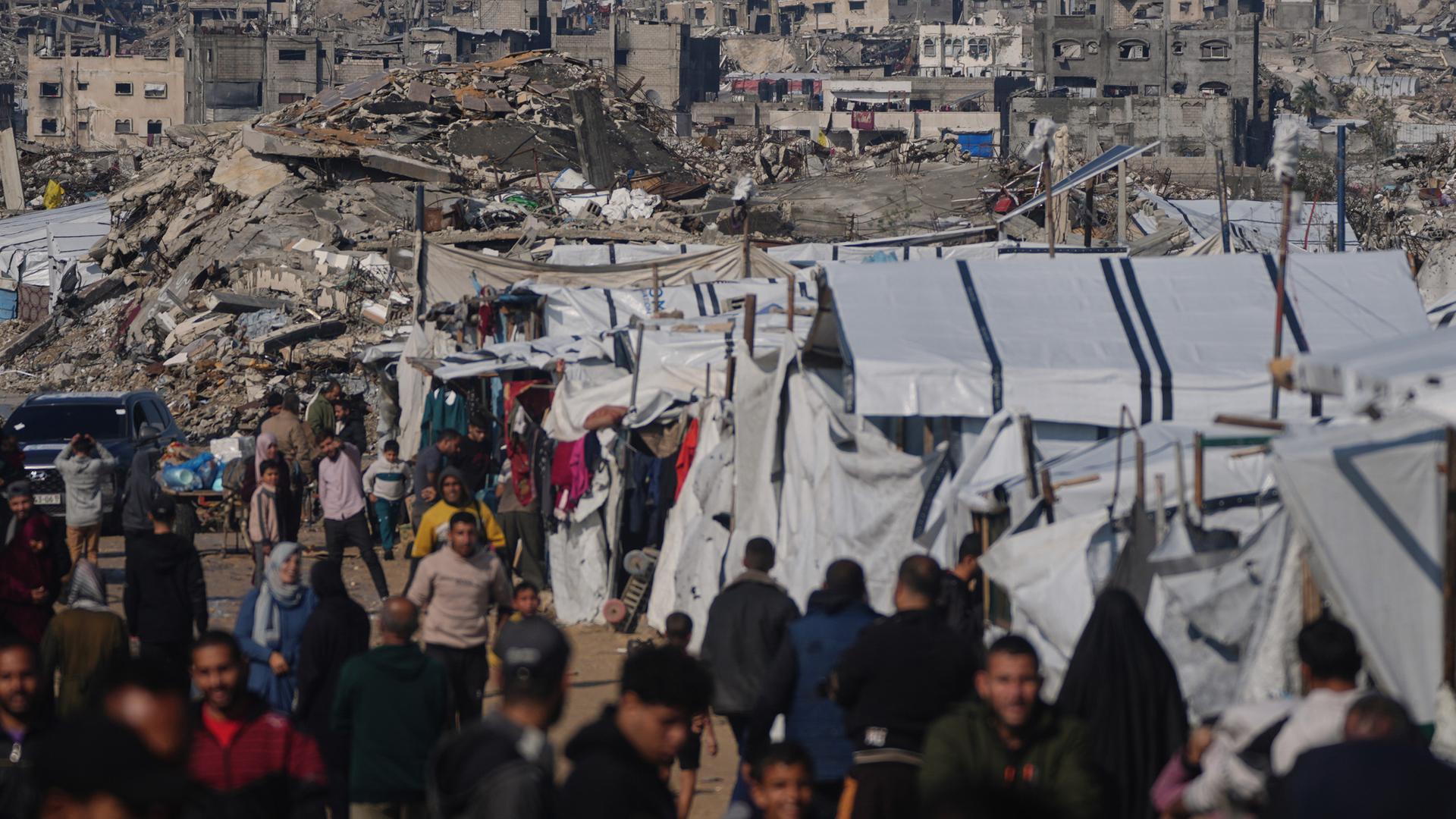 Palästinenser gehen an einem Zeltlager vorbei durch eine Straße in Gaza-Stadt, vor im Hintergrund zerstörten Gebäuden nach israelischen Luft- und Bodeneinsätzen, am 17. Dezember 2025.