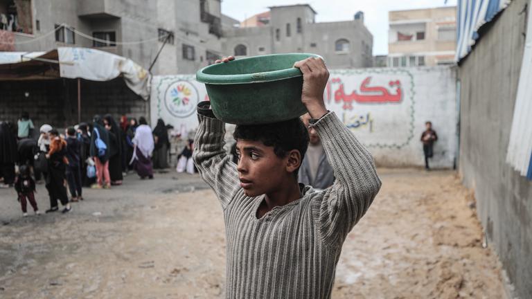 Vertriebene Palästinenser erhalten Mahlzeiten, die von einer Wohltätigkeitsorganisation im Lager Nuseirat verteilt werden, während die Nahrungsmittelkrise aufgrund von Beschränkungen für humanitäre Hilfslieferungen in Deir al-Balah, Gaza, am 13.12.2025 weiter anhält.