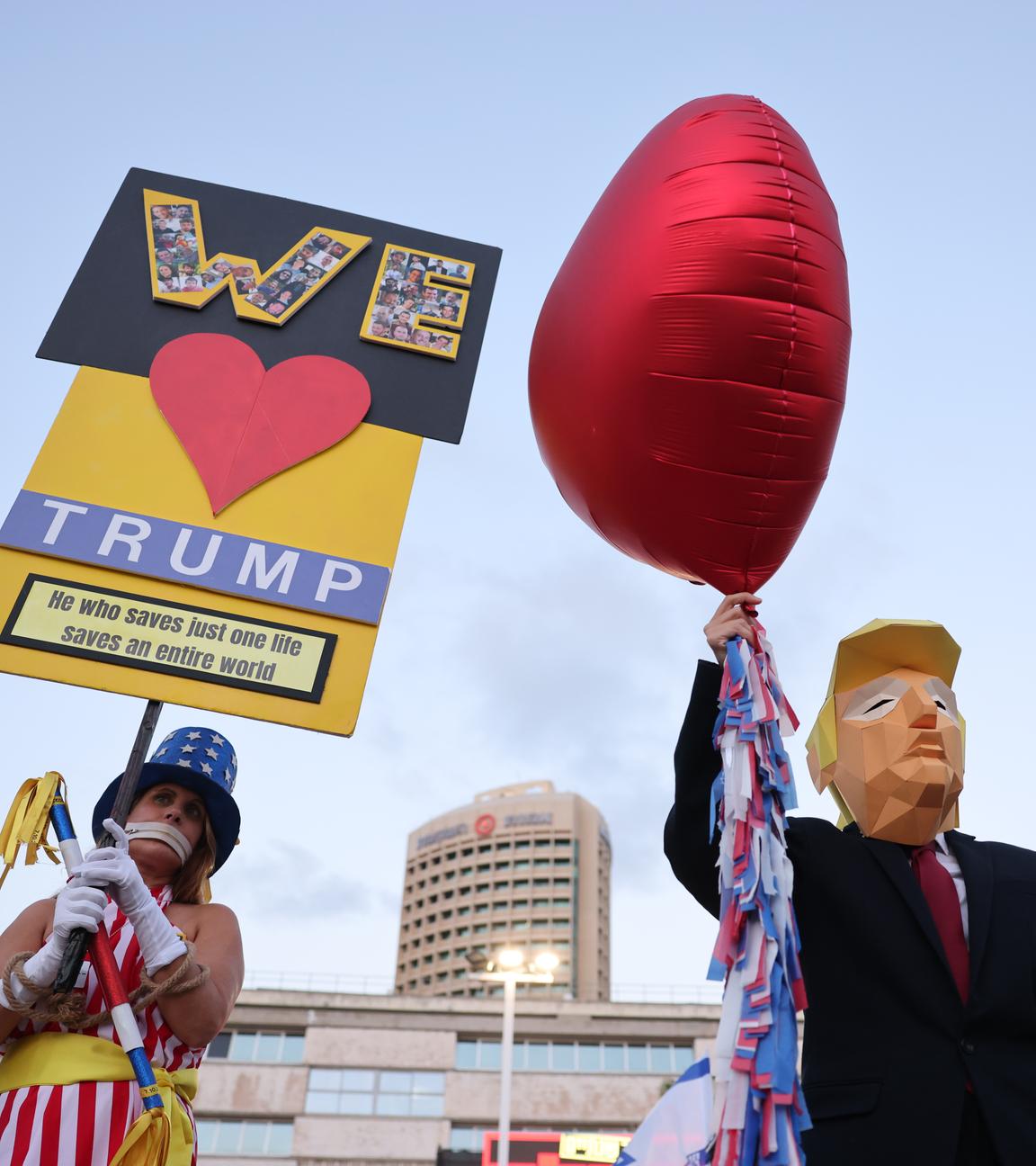 Eine Pappfigur von Trump mit Herz-Luftballon, daneben eine Demonstrantin mit "We Love Trump"-Schild.