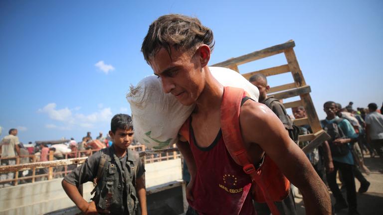 Ein Mann trägt einen Lebensmittelsack auf der Schulter. Er befindet sich am Netzarim-Korridor, wo Lebensmittelvorräte verteilt werden.