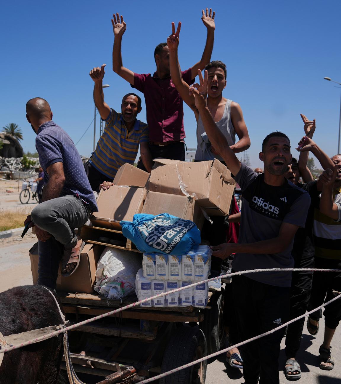 Palästinensische Gebiete, Rafah: Palästinenser winken in die Kamera, während sie Kisten und Taschen mit Lebensmitteln und humanitären Hilfspaketen tragen, die von der Gaza Humanitarian Foundation, einer von Israel anerkannten und von den USA unterstützten Organisation, am Donnerstag, 29. Mai 2025, in Khan Younis im südlichen Gazastreifen geliefert wurden. 