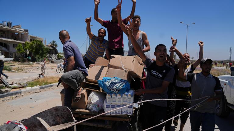 Palästinensische Gebiete, Rafah: Palästinenser winken in die Kamera, während sie Kisten und Taschen mit Lebensmitteln und humanitären Hilfspaketen tragen, die von der Gaza Humanitarian Foundation, einer von Israel anerkannten und von den USA unterstützten Organisation, am Donnerstag, 29. Mai 2025, in Khan Younis im südlichen Gazastreifen geliefert wurden. 