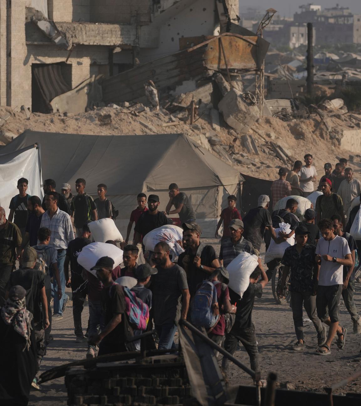 Palästinensische Gebiete, Gaza: Palästinenser tragen Mehlsäcke, die von einem humanitären Hilfskonvoi geliefert wurden, der Gaza-Stadt aus dem nördlichen Gazastreifen erreichte.