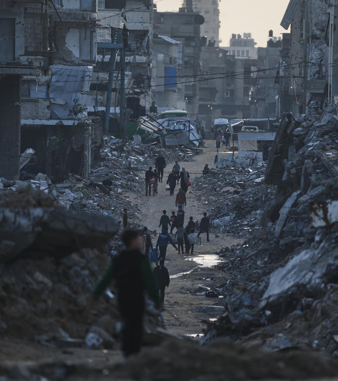 Palästinenser gehen an zerstörten Gebäuden in Gaza-Stadt vorbei.