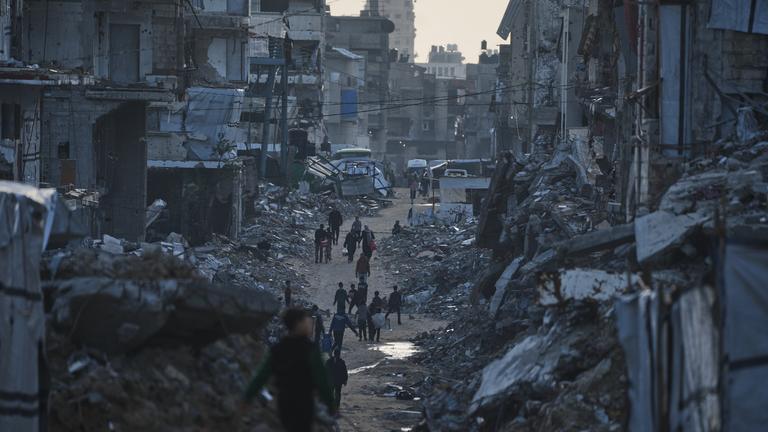 Palästinenser gehen an zerstörten Gebäuden in Gaza-Stadt vorbei.