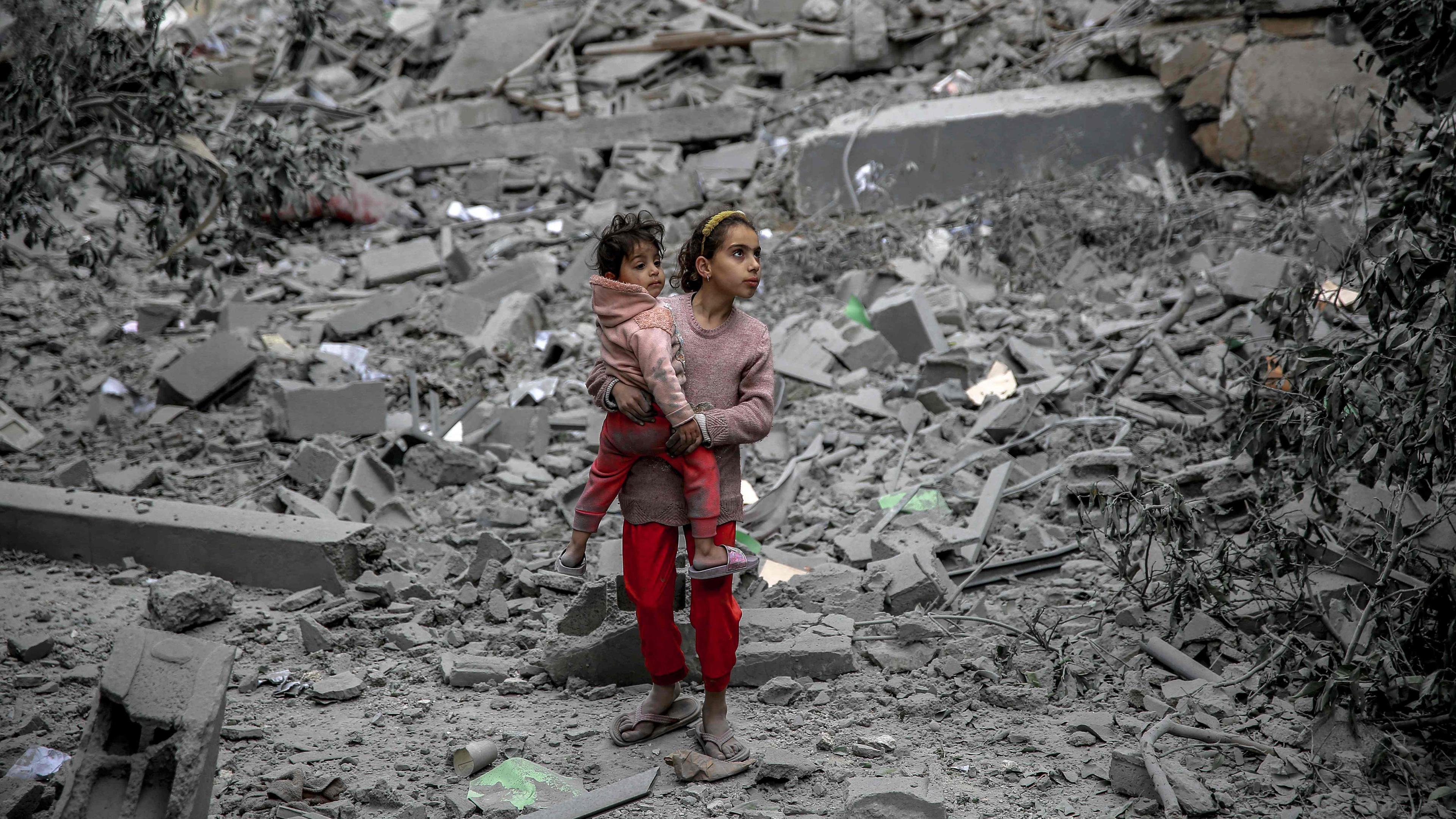 Gaza-Stadt: Ein palästinensisches Mädchen steht inmitten von Trümmern und hält ein kleineres Kind auf dem Arm. 