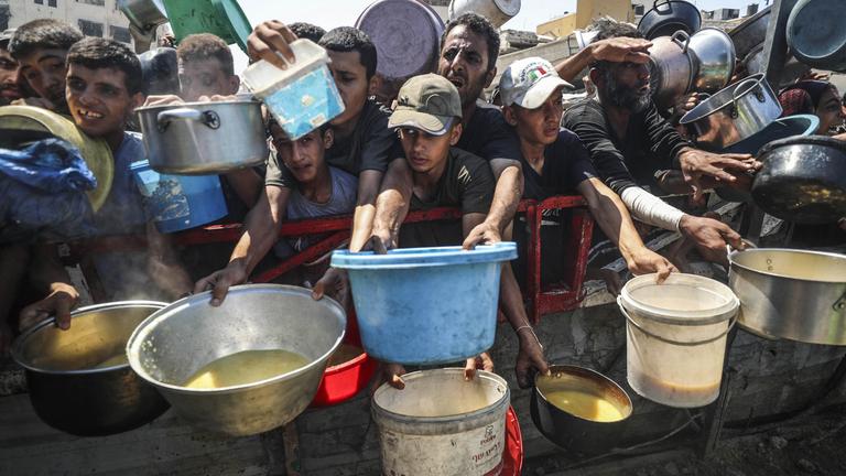 Palästinenser, die Hunger leiden, warten auf eine warme Mahlzeit, an einer Verteilstelle der Welthungerhilfe in Gaza