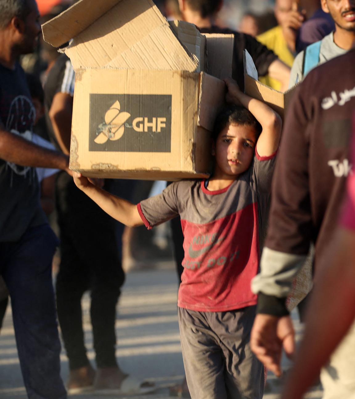 A young boy carrying an aid parcel, walks along the Salah al-Din road near the Nusseirat refugee camp in the northern Gaza Strip, used by food-seeking Palestinians to reach an aid distributution point set up by the privately-run Gaza Humanitarian Foundation (GHF)