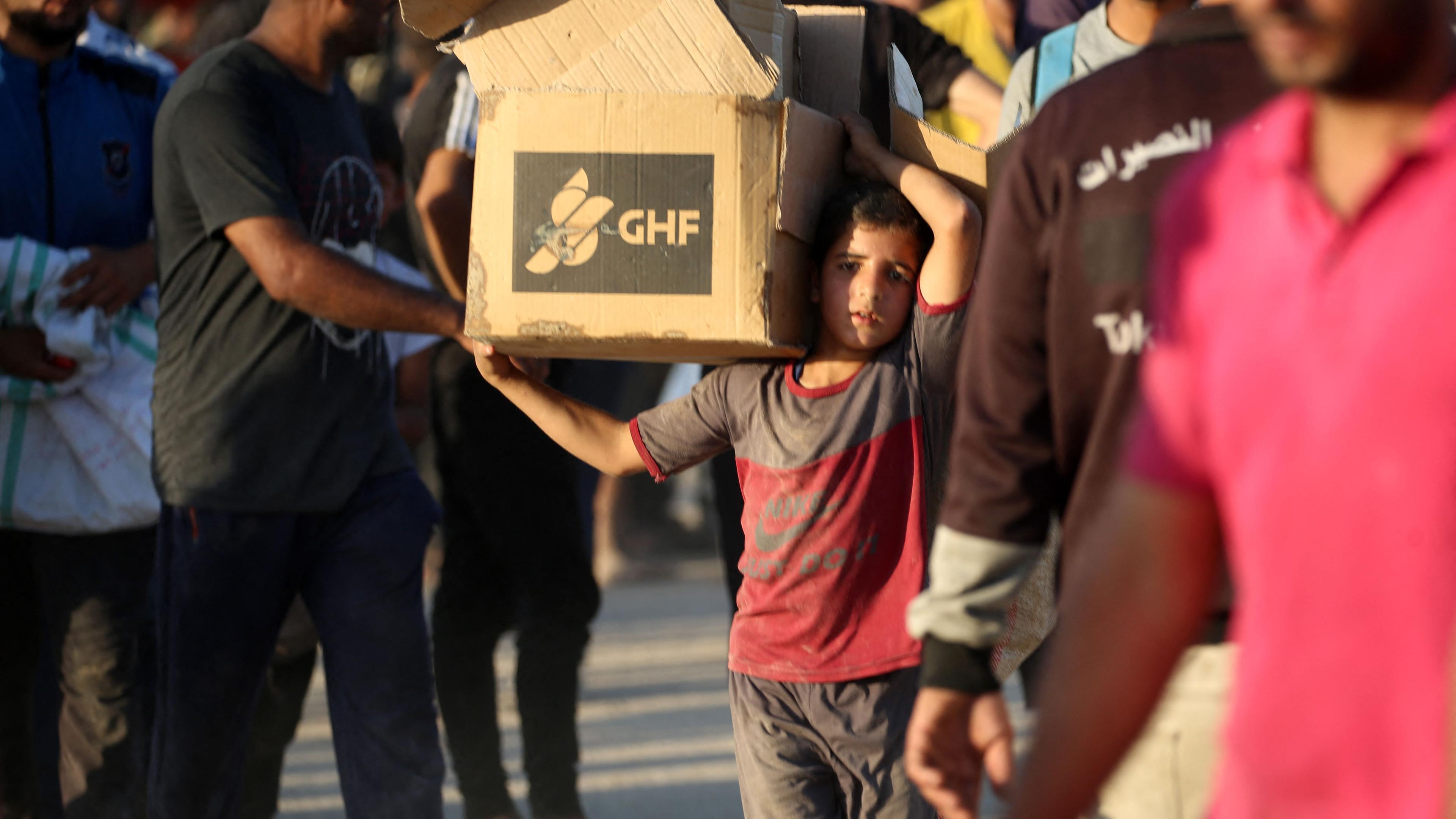 A young boy carrying an aid parcel, walks along the Salah al-Din road near the Nusseirat refugee camp in the northern Gaza Strip, used by food-seeking Palestinians to reach an aid distributution point set up by the privately-run Gaza Humanitarian Foundation (GHF)
