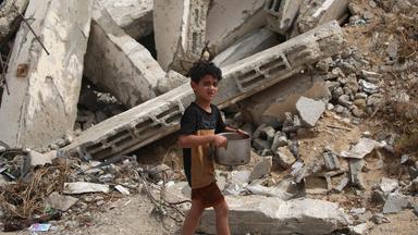 Ein Kind mit einem Topf in den Händen vor einem Schuttberg in gaza.