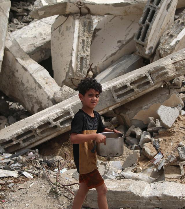 Ein Kind mit einem Topf in den Händen vor einem Schuttberg in gaza.