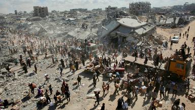 Menschen gehen am 12.10.2025 durch eine stark beschädigte Straße in Khan Yunis im südlichen Gazastreifen. 