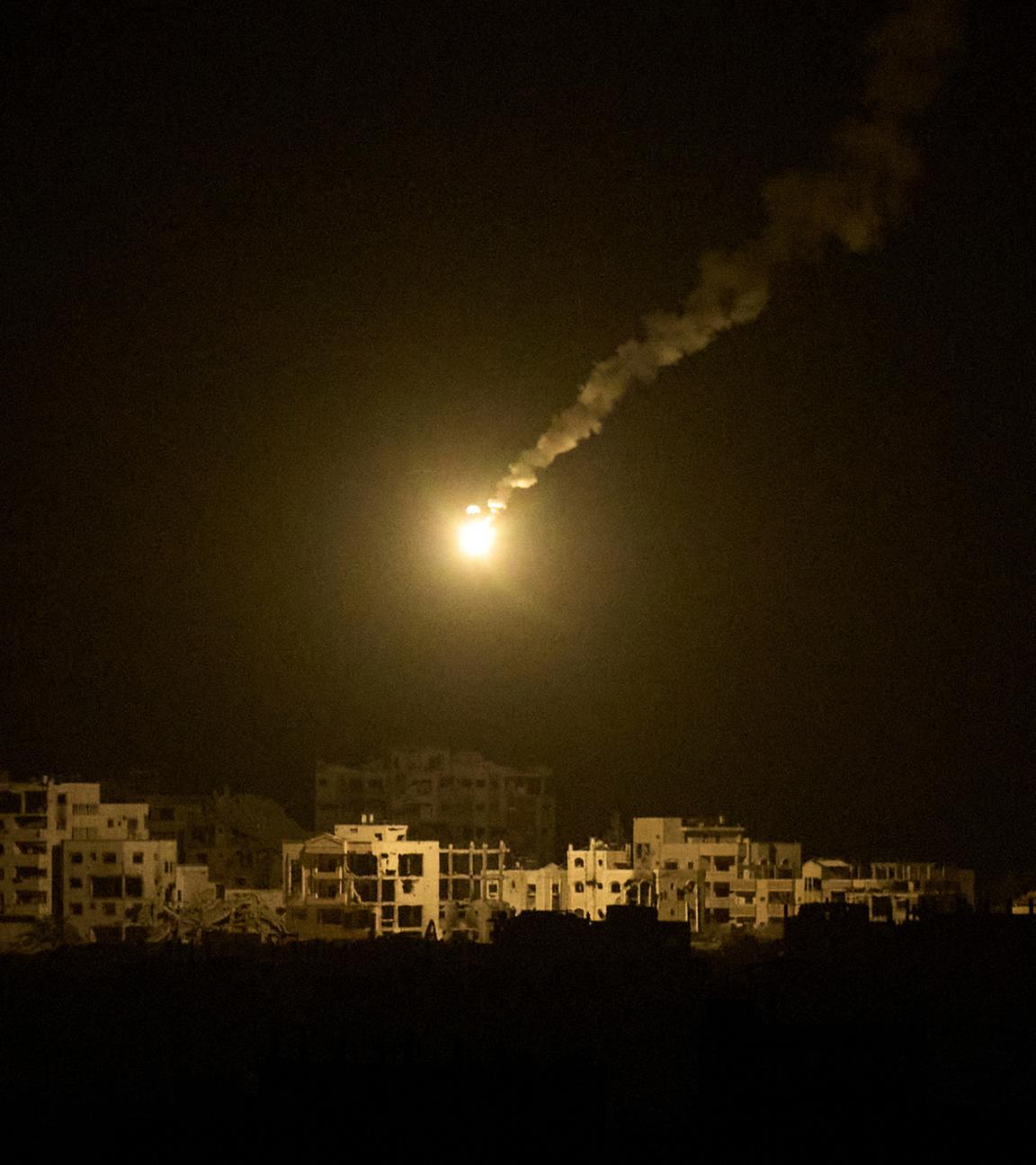 Eine Leuchtrakete der israelischen Armee ist über Gebäuden zu sehen, die während der israelischen Boden- und Luftoperationen im nördlichen Gazastreifen zerstört wurden, gesehen vom Süden Israels aus