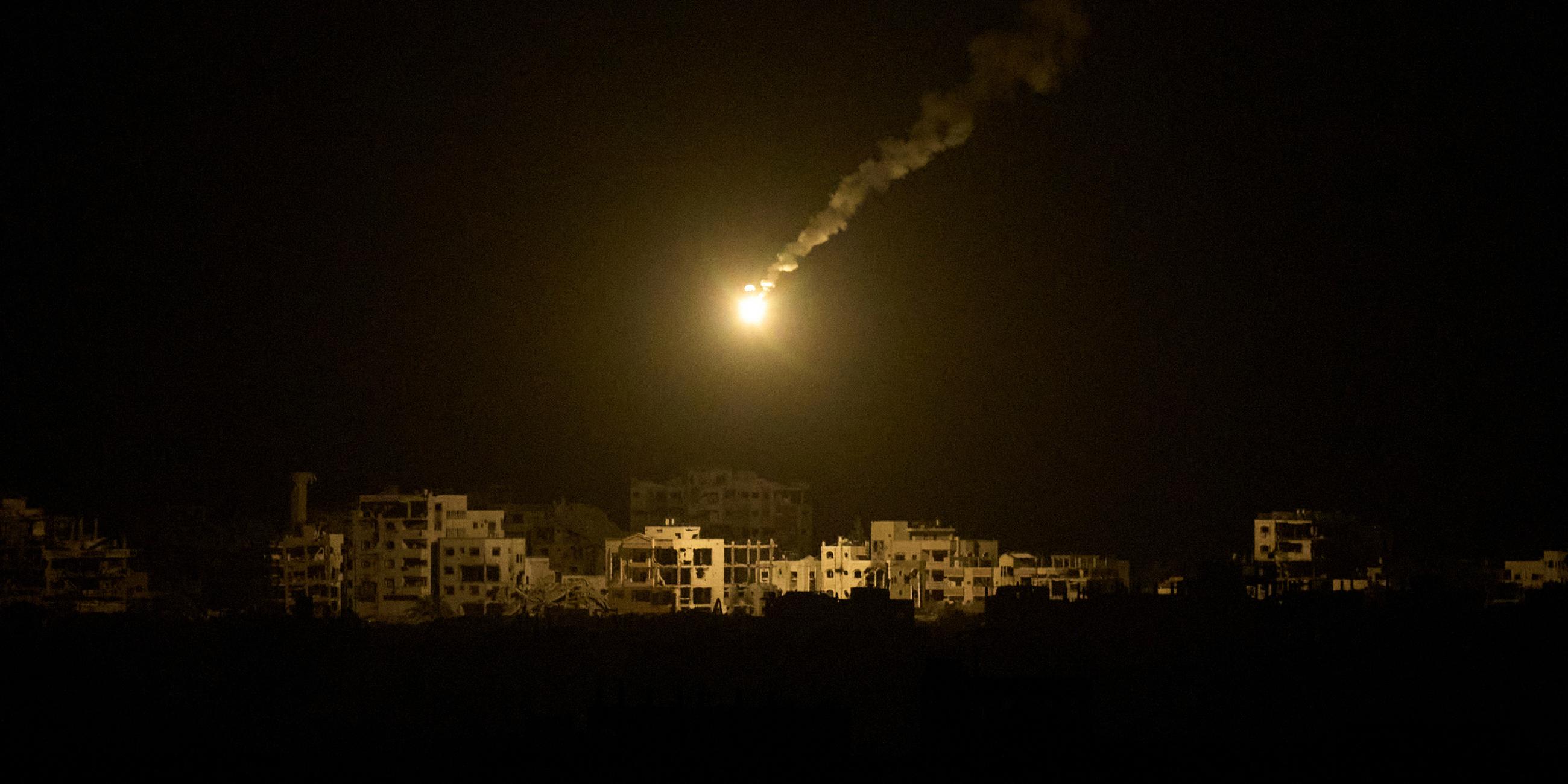 Eine Leuchtrakete der israelischen Armee ist über Gebäuden zu sehen, die während der israelischen Boden- und Luftoperationen im nördlichen Gazastreifen zerstört wurden, gesehen vom Süden Israels aus