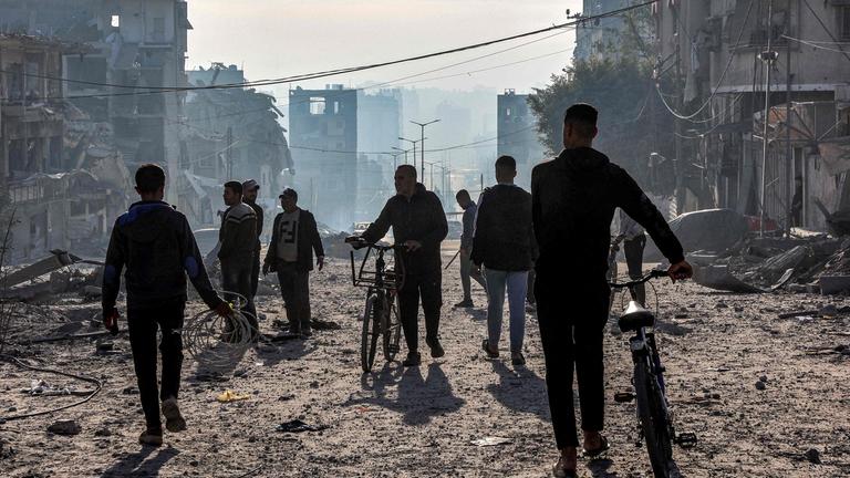 Männer gehen mit Fahrrädern durch Trümmer in in Gaza-Stadt.