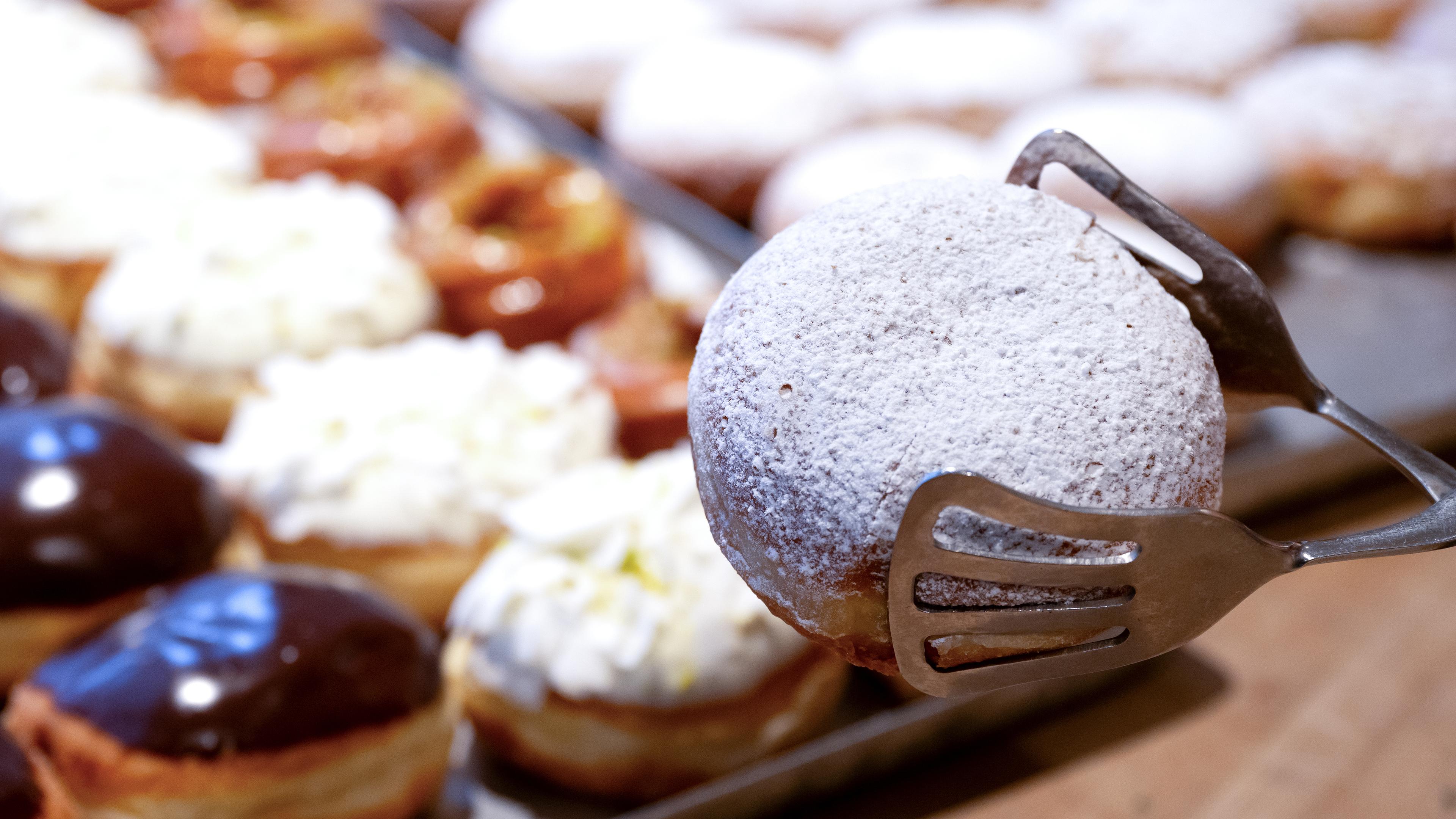 Runde Gebäckstücke - Kräppel oder Berliner - werden mit einer Zange hochgehoben. 