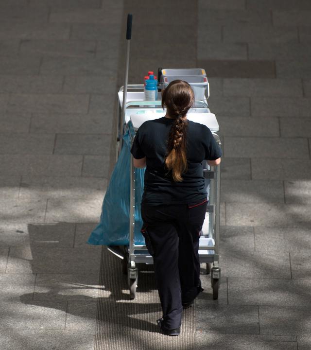 Gebäudereinigerin schiebt Putzwagen vor sich her