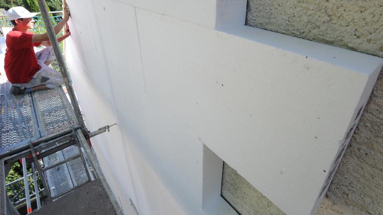 Archiv: Ein Arbeiter befestigt Styroporplatten zur Wärmedämmung an einer Hausfassade