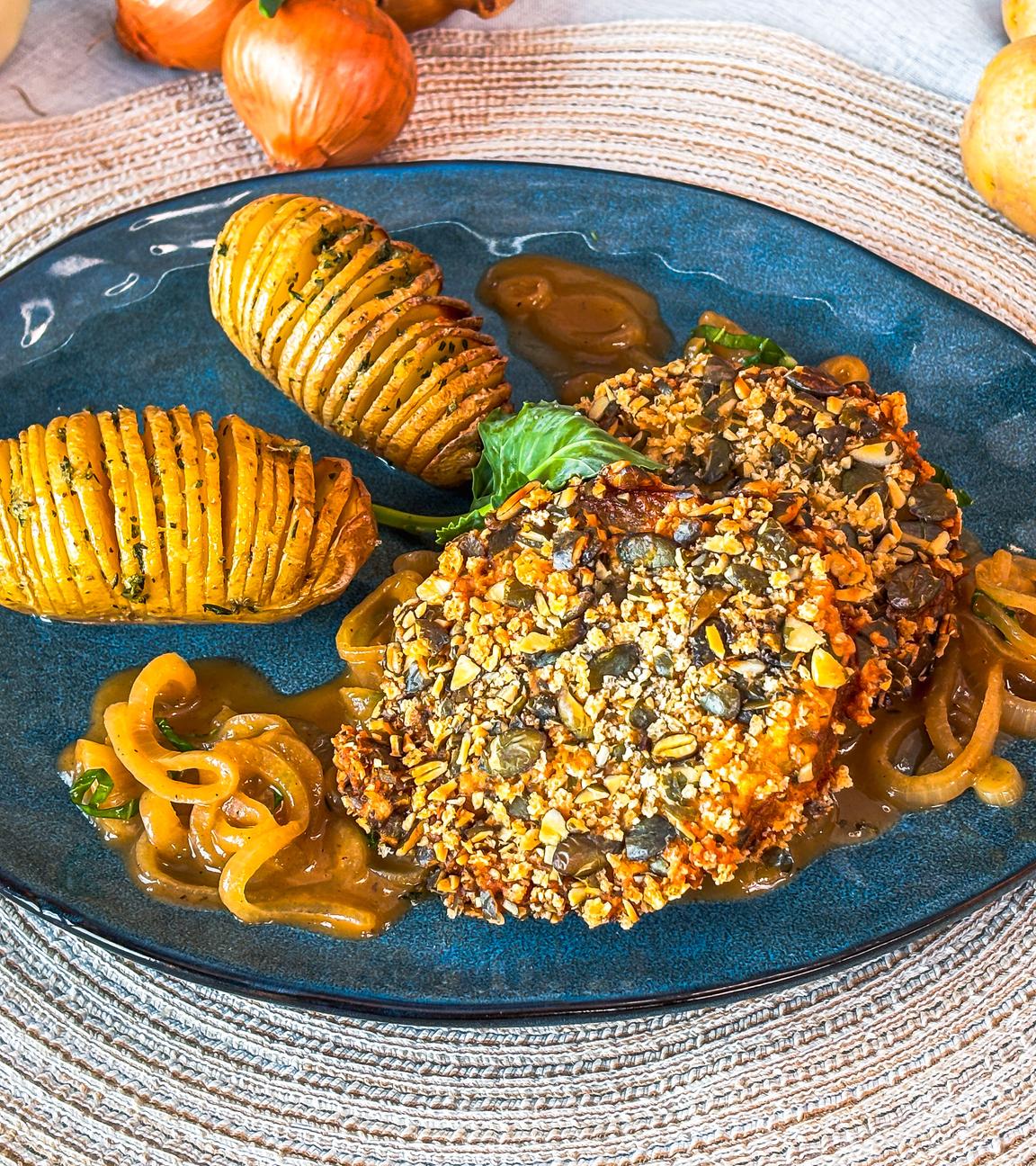 Teller mit gebratenem Kohlrabi im Kürbiskern-Mantel mit Schmorzwiebeln und Fächerkartoffeln.
